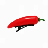 Broche para el pelo con forma de pimiento rojo con detalle de hoja verde, sujetado a una pinza negra.