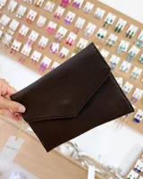 Sobre de fiesta color marrón con textura acanalada y diseño tipo sobre con solapa triangular. Incluye una correa de mano pequeña.