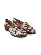 Mocasines de cuero con pelo, con estampado de manchas tipo vaca en tonos marrón y blanco. Presentan un diseño clásico de mocasín con antifaz y suela plana de goma negra.