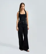 Pantalón wide leg de denim negro con acabado desgastado, tiro medio y aplicación de tachas metálicas a lo largo de los laterales.