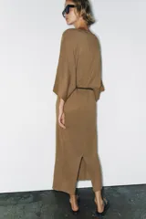 Vestido midi de punto color marrón con escote en V, mangas anchas y diseño holgado. Incluye un cinturón delgado marrón con hebilla metálica.