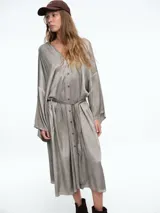 Vestido tipo camisero de corte midi, con cierre frontal de botones, mangas largas amplias y lazo ajustable en la cintura. Presenta un acabado desgastado en tono gris.