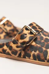 Zueco destalonado de cuero vacuno con estampado de leopardo. Presenta una tira ancha con hebilla metálica dorada sobre el empeine.