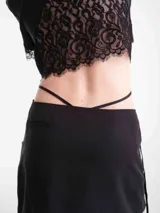 Camisa crop negra de tencel, con mangas cortas y detalles de encaje en el cuello, la botonera frontal, el dobladillo inferior y las mangas. Cuenta con tiras ajustables que se atan alrededor de la cintura.