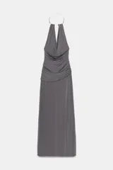 Vestido largo de color negro con cuello halter y detalle de aro metálico en el escote. Presenta un diseño drapeado en la parte frontal y escote en pico pronunciado.