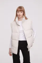 Chaleco acolchado color marfil con cuello alto y cierre frontal con botones a presión.