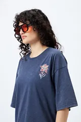 Remera negra de corte holgado con mangas cortas amplias y cuello redondo. Estampado pequeño de flor en el pecho y estampado grande en la espalda con diseño floral y texto.