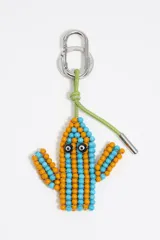 Llavero con dije en forma de cactus, confeccionado con cuentas (beads) de colores naranja y azul claro, con dos ojos negros. Se sujeta mediante un mosquetón metálico plateado y un cordón trenzado de cuero sintético verde lima.
