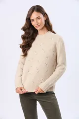 Buzo tejido de punto en color beige, con cuello redondo, mangas largas y puños acanalados. Presenta un delicado diseño bordado con motivos florales dispersos en el frente y una etiqueta de cuero sintético en el ruedo.