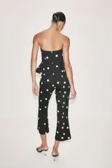 Mono largo de escote recto sin tirantes, con peplum en la cintura, perneras acampanadas y estampado de lunares.