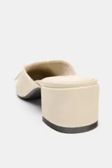 Zapatos de tacón tipo bailarina destalonada en piel color beige, con detalle de lazo en la parte delantera, tacón en bloque y punta redonda.