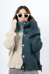 Saco de hilo con cuello alto y cierre de botones, de tejido de punto y diseño oversize. Presenta un teñido artesanal degradado que combina gris y beige, con mangas largas y puños amplios, además de un detalle de aplicación floral oscura en el pecho.