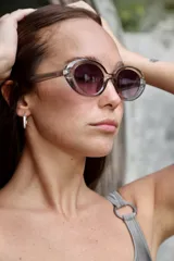 Lentes de sol con montura ovalada color gris translúcido y cristales degradados en tonos de violeta.