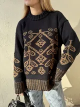 Buzo de tejido de punto pesado, color negro con diseño geométrico y floral en color marrón. Presenta cuello redondo, mangas largas y puños y ruedo acanalados con detalle de rayas en contraste.