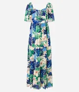 Vestido largo de viscosa con estampado tropical de flores blancas y hojas verdes y azules. Presenta escote cuadrado con lazo ajustable en el centro del busto y mangas cortas abullonadas. La falda es escalonada con volados.