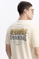 Remera de manga corta color beige, con escote redondo y ajuste regular. Presenta un estampado en la espalda con la frase "POSITIVE THINKING" en letras doradas y negras, y el logo de Mistral.