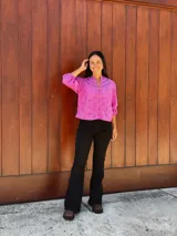 Camisa fucsia de tela con perforaciones tipo broderie, de corte holgado, cuello redondo con pequeña abertura en V, cierre frontal con botones y mangas tres cuartos con puños elásticos.