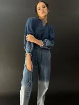 Mono largo de jean azul con lavado artesanal, escote en V regulable con cierre invisible, mangas largas abullonadas y lazo en la cintura.