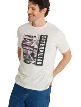 Remera de algodón color beige con cuello redondo y mangas cortas. Cuenta con un gran estampado gráfico frontal en tonos oscuros con la inscripción 'Power For' y 'Caterpillar', acompañado de una ilustración de maquinaria e infraestructura industrial.