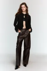 Chaqueta de punto negra con cuello redondo, manga larga y flecos en el bajo y los puños. Cierre frontal con un botón dorado.