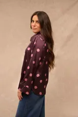Camisa de satén color bordó con estampado de lunares rosados, cuello camisero, cierre frontal con botones y mangas largas con puños anchos.