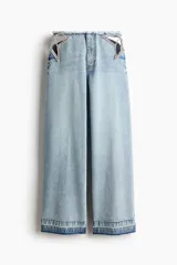 Jean de pierna recta en denim de algodón rígido, con diseño de aberturas laterales en la cintura decoradas con cristales brillantes. Presenta un corte holgado, cintura con borde desflecado y bajo deshilachado.