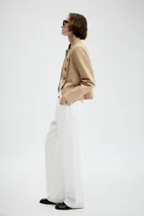 Blazer entallado de sarga color beige con cuello subido y escote en pico. Presenta manga larga con hombreras, detalle de botones metálicos decorativos en el frente y cierre frontal con gancho metálico. Incluye falsos bolsillos de vivo y abertura en la espalda.