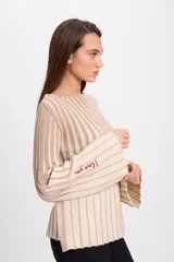 Sweater de punto con diseño de rayas verticales en dos colores, azul y crudo. Presenta cuello bote, mangas largas con terminación acampanada y un aplique decorativo en el pecho.