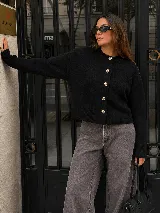 Cardigan negro de tejido de punto con cuello redondo, manga larga y cierre frontal de botones dorados metálicos grabados.
