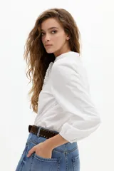 Camisa de algodón color blanco con cuello mao, mangas largas abullonadas con puños elásticos y detalle de volados en la parte frontal. Cuenta con cierre de botones de nácar.