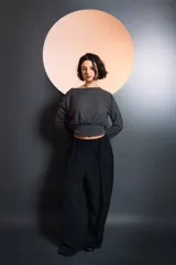Top de manga larga en tejido de punto acanalado color gris oscuro, con diseño cruzado en el frente y cintura ajustada con elástico. Presenta un detalle bordado en la parte inferior.