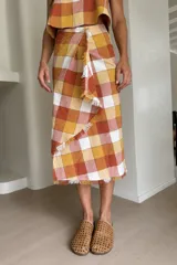 Falda midi a cuadros con diseño cruzado, cierre de botón en la cintura y terminaciones desflecadas en los bordes.