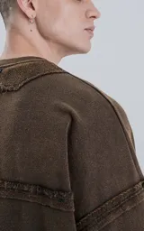 Buzo de cuello redondo color marrón oscuro con efecto desgastado (lavado óxido). Presenta costuras expuestas y detalles de pespunte ondulado en puños y ruedo. Tiene un calce oversize y crop.