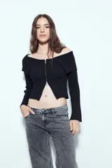 Top de punto acanalado negro, con diseño off-shoulder y escote amplio. Presenta mangas largas y cierre frontal completo con doble cursor, permitiendo ajustar la apertura superior e inferior.