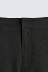 Bañador de hombre color negro, de largo medio, confeccionado en tejido técnico. Presenta cintura elástica ajustable con cordón interior, trabillas laterales, bolsillos frontales y bolsillo trasero con cierre de cremallera.