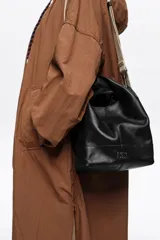 Bolso de mano Bimba y Lola modelo Paper mediano, confeccionado en cuero color tostado con estructura blanda, asas superiores y correa de hombro ajustable en color beige. Presenta costuras visibles, logo metálico de la marca en la parte inferior y cierre principal.