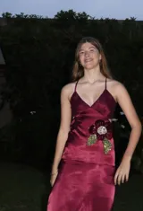 Vestido largo bordó de satén con escote en V, tirantes finos cruzados en la espalda, aberturas laterales (cut out) en la cintura y un aplique floral decorativo.