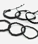 Set de seis pulseras de estilo casual, todas en color negro. Incluye tres pulseras trenzadas ajustables con cordón y tres pulseras con cuentas elásticas (algunas de cuentas lisas y otras de cuentas texturizadas).