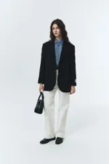 Blazer negro de lana con calce overfit y estética vintage. Presenta cierre frontal de dos botones, bolsillos exteriores y botones de cuerno natural grabados con logo.