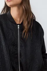 Campera bomber de textura satinada con cierre frontal de cremallera, cuello redondo y mangas largas con puños elásticos.