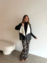 Chaleco de cuero sintético con solapas amplias forradas en corderito sintético blanco. Presenta un diseño abierto sin cierre frontal, ideal para superponer sobre vestidos.