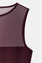 Body sin mangas de cuello redondo, confeccionado en una combinación de tul transparente y paneles de tela opaca a tono. Presenta un diseño ajustado con cierre inferior mediante botones a presión.
