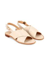 Sandalia plana de cuero beige con tiras anchas cruzadas en el empeine, tira trasera con hebilla metálica ajustable y suela baja con pequeño tacón.