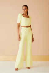 Pantalón amarillo de tiro alto y corte acampanado, con bolsillos frontales con cierre dorado.