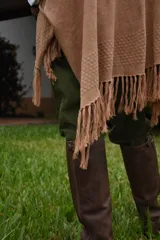 Ruana de hilo de algodón color beige con terminación de flecos en los extremos y pequeño detalle de etiqueta lateral.