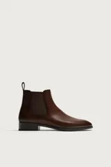 Bota Chelsea de hombre en color marrón oscuro, con diseño liso, punta afilada, elásticos laterales y tirador trasero.