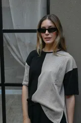 Remera de tejido de punto, manga corta, con diseño bicolor en negro y beige. La prenda es de corte holgado y presenta un ligero acanalado vertical.