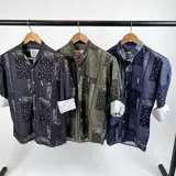 Camisa negra de cuello mao con estampado de arabescos en blanco y logo de la marca bordado en el pecho. Mangas largas con puños abotonados y corte clásico.