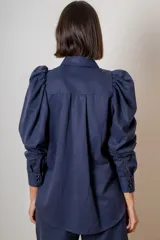 Camisa de algodón color marrón con mangas largas abullonadas, cuello clásico y cierre frontal oculto. Presenta botones decorativos con strass en los puños y en el cuello.