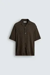 Camisa de corte relajado con cuello bowling y manga corta. Confeccionada en tejido fluido con textura jacquard de patrón geométrico y cierre frontal de botones.